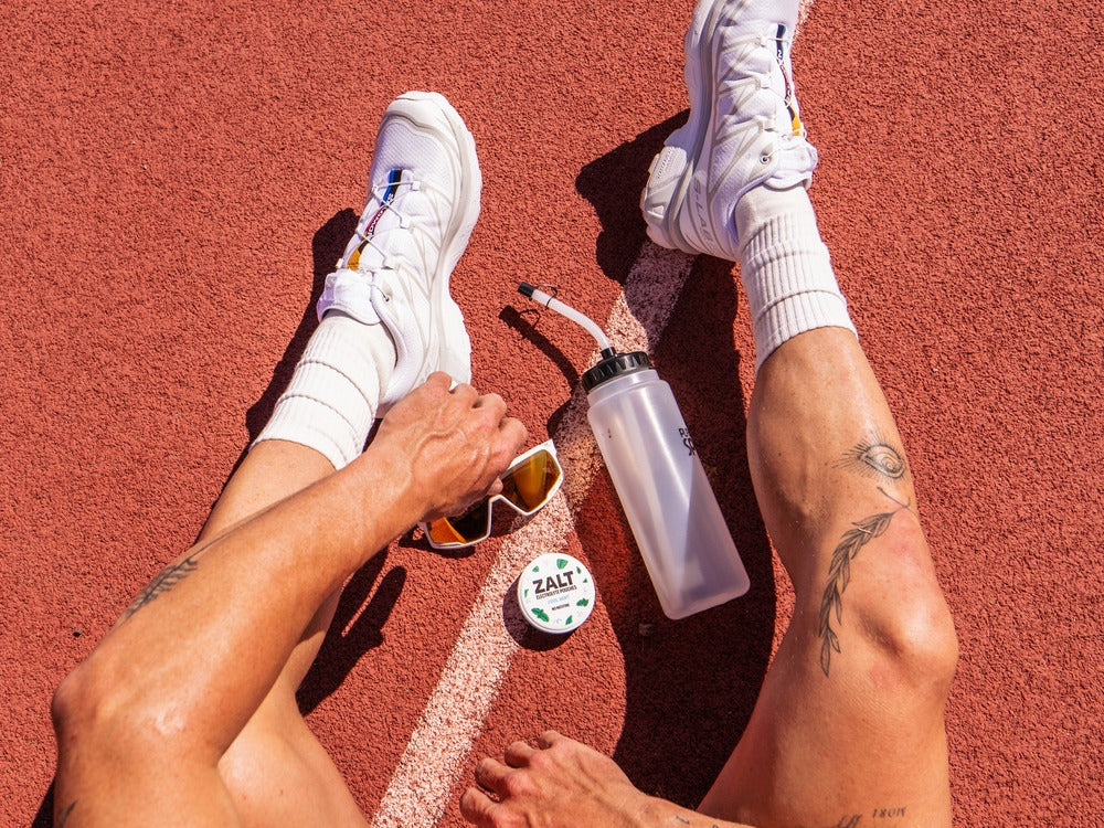 Sneakers on a running track beside a water bottle and a tin of ZALT