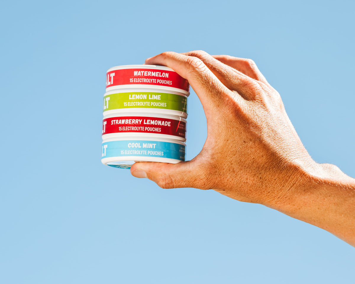 A hand holding a stack of ZALT electrolyte pouch cans: Watermelon, Lemon Lime, Strawberry Lemonade, and Cool Mint